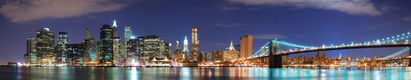 نمای چشم‌انداز افق شهر نیویورک منهتن با پل بروکلین و ساختمان‌های آسمان‌خراش اداری در هنگام غروب روشن شده با چراغ‌ها در شب