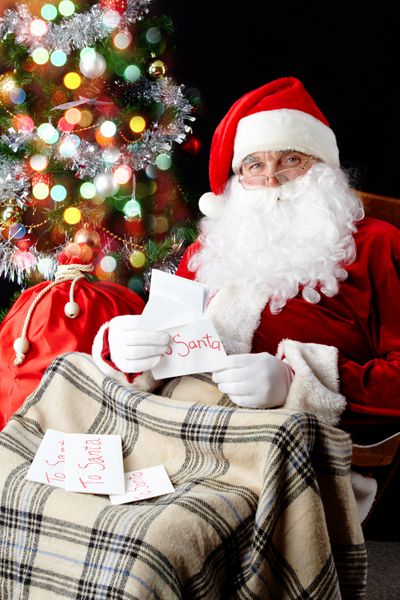 بابا نوئل پشت درخت کریسمس نشسته و نامه های کریسمس را می خواند