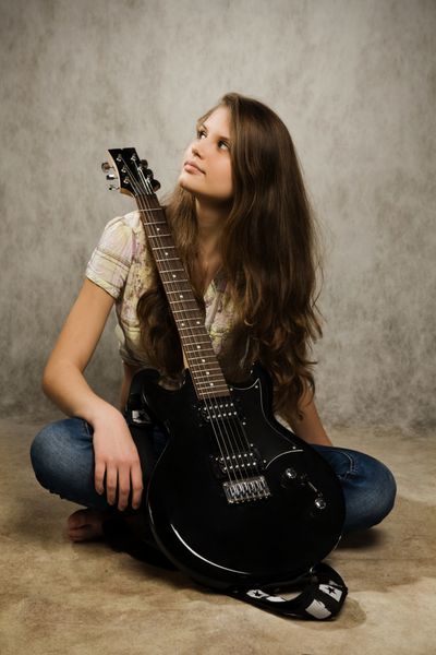 دختر نوجوان پاچه‌دار با گیتار الکتریک در پس زمینه خاکستری
