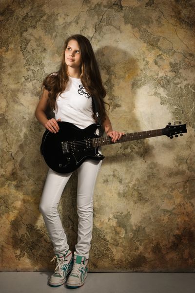 دختر نوجوان با گیتار الکتریک در پس زمینه دیوار