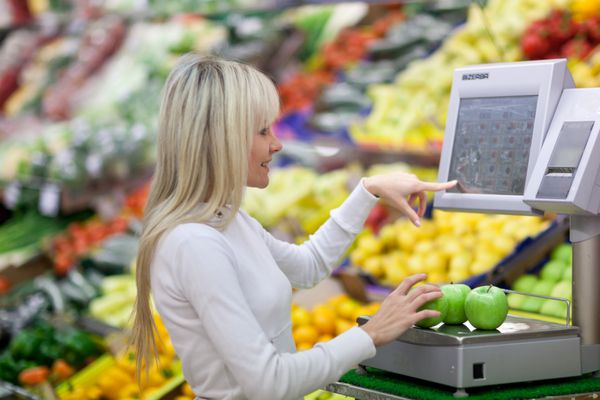 زن جوان زیبا در حال خرید میوه و سبزیجات در بخش محصولات یک سوپر مارکت خواربار فروشی کم عمق