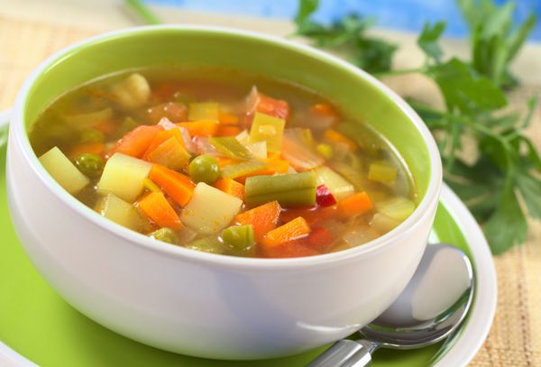 سوپ سبزیجات تازه از لوبیا سبز نخود هویج سیب زمینی فلفل دلمه ای قرمز گوجه فرنگی و تره فرنگی در کاسه ای با جعفری در پشت تمرکز انتخابی تمرکز روی سبزیجات یک سوم در سوپ