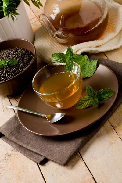 چای نعناع سبز خوشمزه در فنجان شیشه ای روی میز چوبی