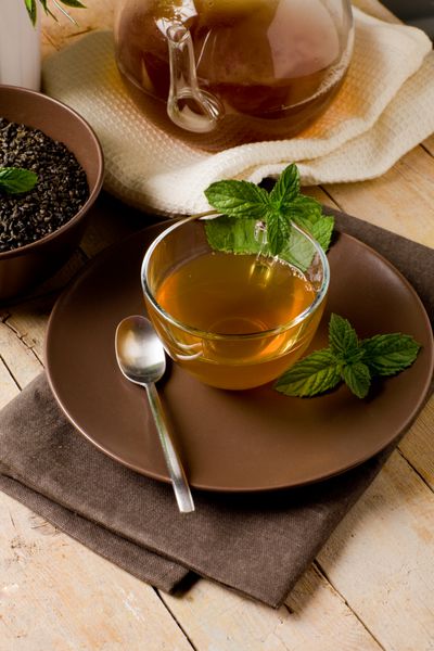 چای نعناع سبز خوشمزه در فنجان شیشه ای روی میز چوبی