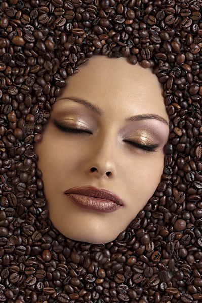 نمای نزدیک از یک دختر غوطه ور در دانه های قهوه و چشمانش را بسته نگه می دارد