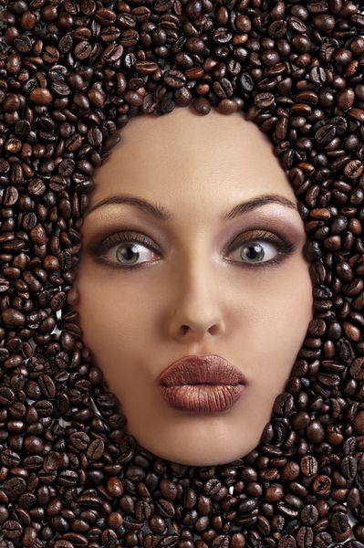 نمای نزدیک از یک دختر غرق شده در دانه های قهوه در حال دمیدن بوسه