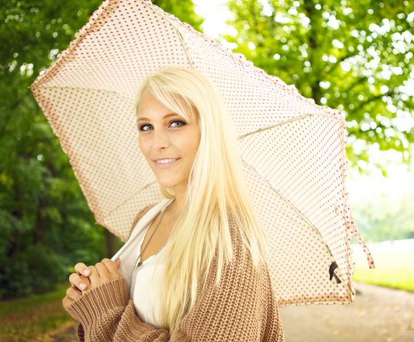 دختر زیبای سینه دار جوان با چتر زیر درختان در پارک
