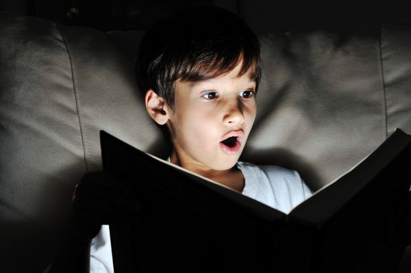 کودک در حال خواندن کتاب نور در تاریکی
