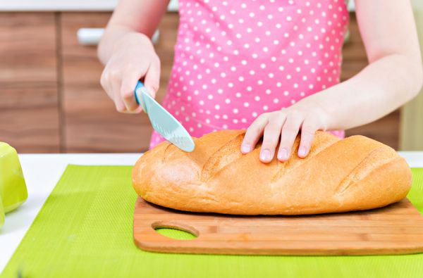 دختر کوچولو با پیش بند صورتی در حال بریدن نان