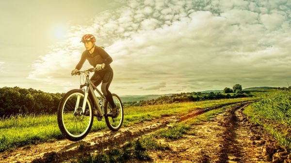 زن دوچرخه سواری ورزشی در یک چمنزار با چشم انداز زیبا