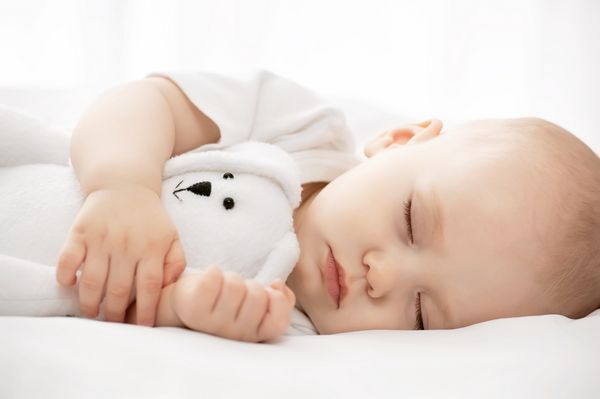 خواب بی دغدغه کودک کوچولو با یک اسباب بازی نرم روی تخت