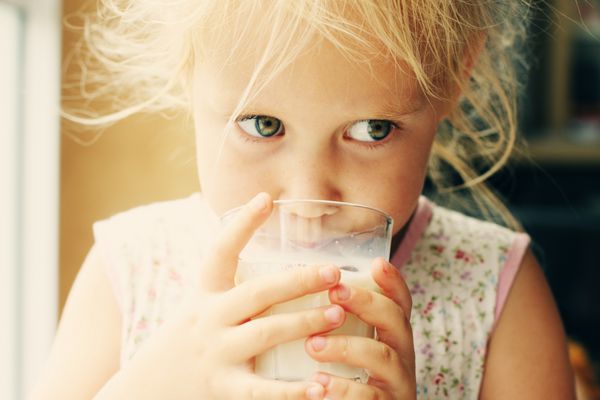 دختر کوچولوی شاد و ناز در حال نوشیدن شیر