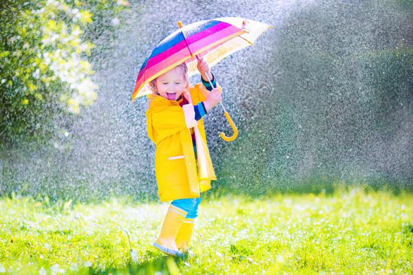 کودک نوپا بامزه با چتر در حال بازی در باران