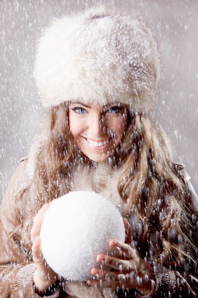 زن جوان زیبا که یک توپ برفی در دست دارد