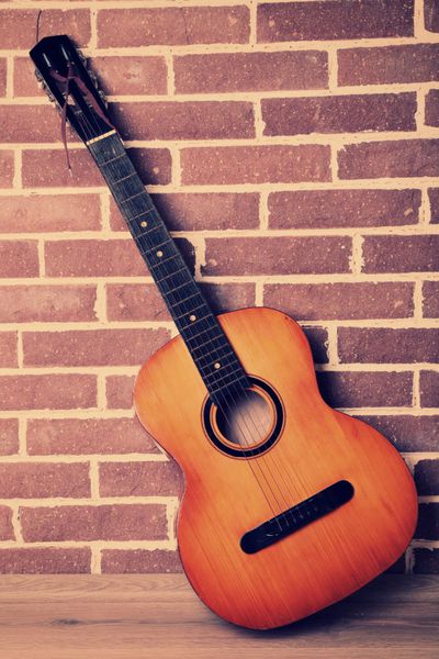 گیتار روی زمین در پس زمینه دیوار آجری