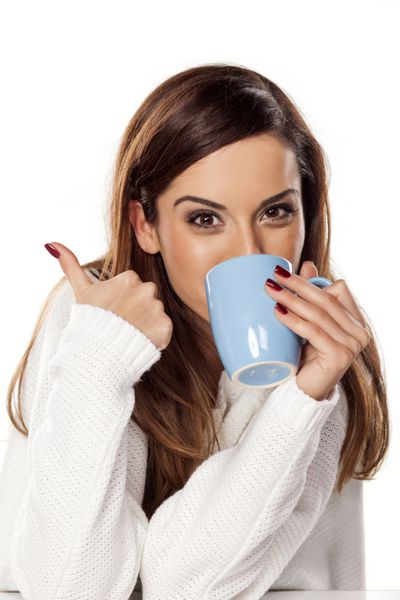 زن جوان زیبا که یک فنجان چای در دست دارد و شست را نشان می دهد