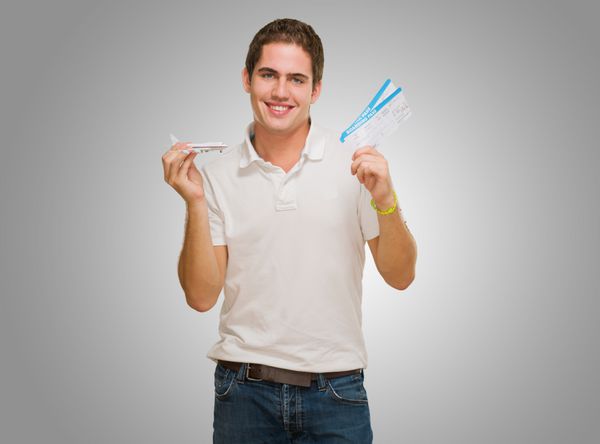 مرد جوانی که کارت پرواز و هواپیمای اسباب بازی را در پس زمینه خاکستری در دست دارد