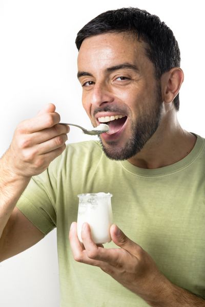 مرد جوان شاد با ریش در حال خوردن ماست جدا شده در پس زمینه سفید