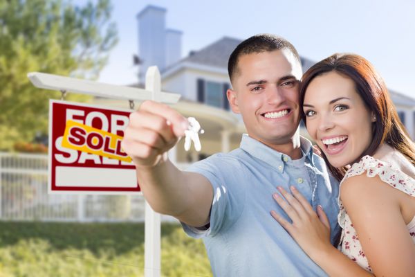 زوج نظامی هیجان زده در مقابل خانه جدید با کلیدهای خانه جدید و فروش تابلو املاک بیرون