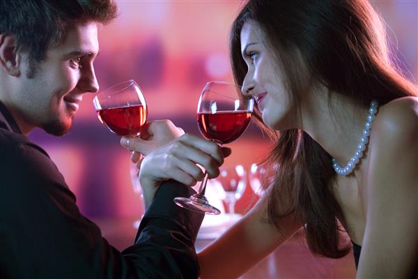 زوج جوانی که در رستوران جشن یا قرار عاشقانه یک لیوان قرمز به اشتراک می گذارند