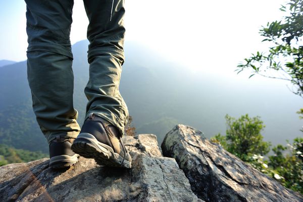 پاهای زن کوهنورد روی قله کوه ایستاده است