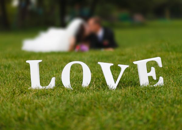 زوج عروسی بدون تمرکز و کلمه عشق سفید بزرگ روی چمن