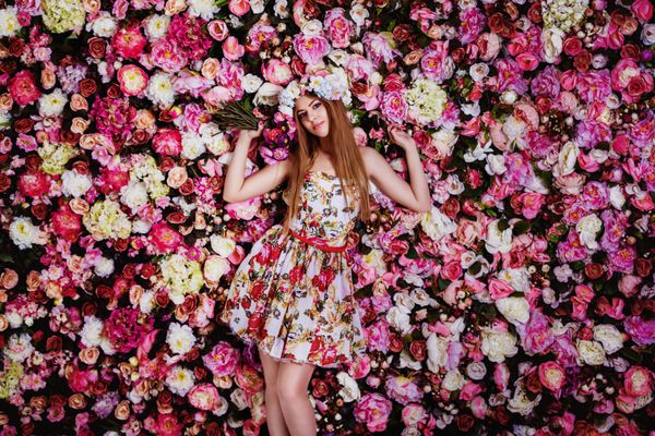 یک دختر جوان زیبا با دسته گل در نزدیکی یک دیوار گلدار