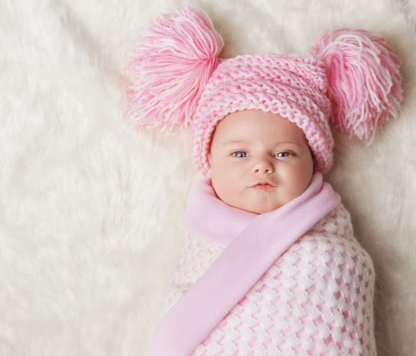 دختر بچه پیچیده شده در پتوی نوزادی کلاه همراه بچه تازه متولد شده یک ماهه روی فرش