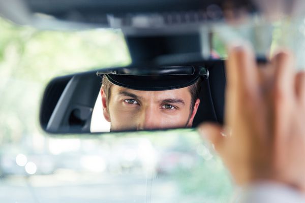 راننده مردی که در ماشین نشسته و به انعکاس خود در آینه نگاه می کند