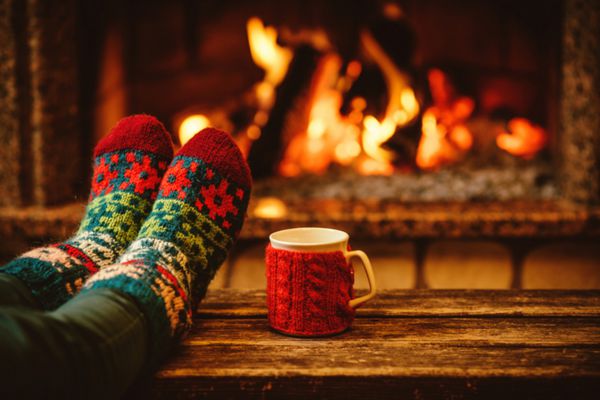 پاها در جوراب های پشمی در کنار شعله کریسمس زن با یک فنجان نوشیدنی و گرم کردن پاهای خود در جوراب های پشمی در کنار آتش گرم استراحت می کند نزدیک روی پا مفهوم تعطیلات زمستانی و کریسمس
