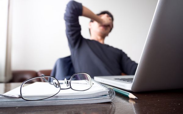 مردی با دستش که f خود را گرفته و از کار با لپ تاپ و نوت بوک با عینک روی میز چوبی ترمز می گیرد مفهوم استرس استراحت تنش شکست خورده افسردگی اشتیاق