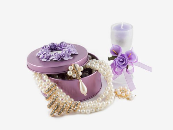 گردنبند و گوشواره طلایی زیبا و زیبا در جعبه سنگ بنفش و شمع معطر در شیشه تزئین شده با گل های مصنوعی در زمینه سفید
