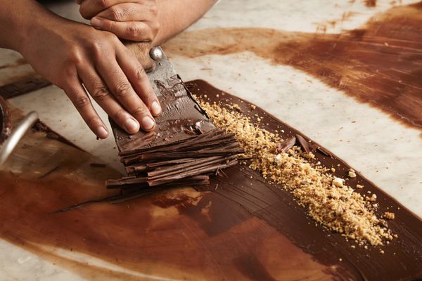 از نزدیک رئیس مرد سیاه‌پوست حرفه‌ای دایره‌های آشپزی از شکلات آب‌شده خانگی روی میز مرمر سنگی در نانوایی