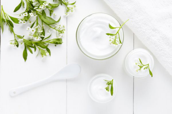 کرم بهداشتی آرایشی درماتولوژی گیاهی با محصول مراقبت از پوست گل در ظرف شیشه ای در زمینه سفید