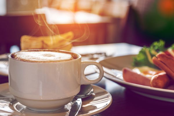 نمای نزدیک از فنجان قهوه با صبحانه در کافی شاپ
