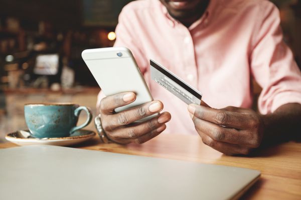 مرد آفریقایی آمریکایی با پیراهن دستی که با کارت اعتباری آنلاین پرداخت می کند در حالی که از طریق اینترنت سفارش می دهد تاجر سیاه پوست موفقی که با استفاده از اپلیکیشن موبایل بانک معامله می کند تمرکز انتخابی