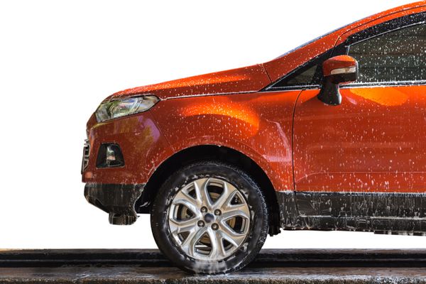 ماشین نارنجی با صابون سفید روی بدنه در فروشگاه مراقبت از ماشین جدا شده در زمینه سفید