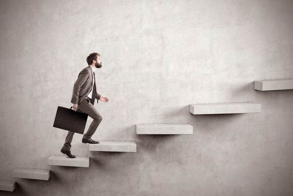 نمای جانبی مردی در حال بالا رفتن از پله‌های ساخته شده در یک دیوار بتنی خالی مفهوم موفقیت و رسیدن به هدف مدل آزمایشگاهی ماکت