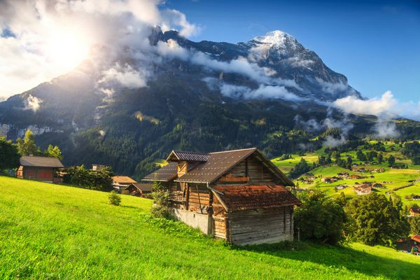 خانه های چوبی کوهستانی افسانه ای مزارع سرسبز و شهر توریستی معروف گریندل والد با ارتفاعات شمالی کوه های ایگر برنز اوبرلند سوئیس اروپا