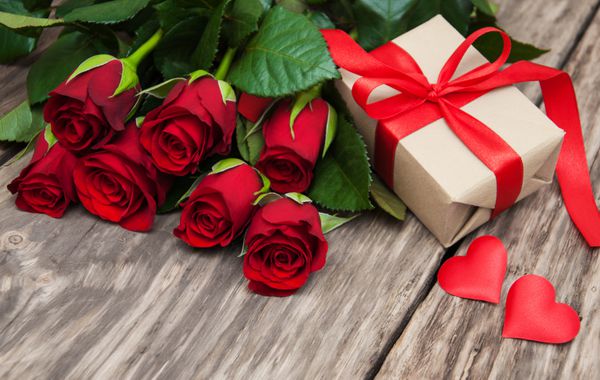 گل رز قرمز و جعبه هدیه روی میز چوبی