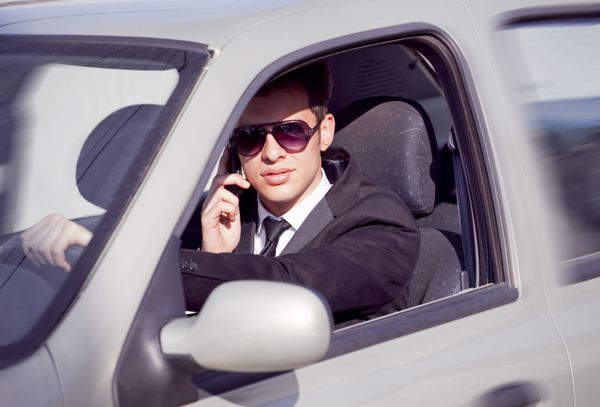 تاجر جوان در ماشینش پشت فرمان در حال صحبت با تلفن همراه