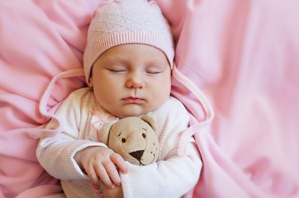 خواب نوزاد ناز با اسباب بازی خرس عروسکی روی تخت نرم صورتی در خانه