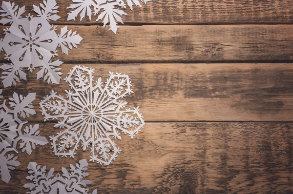 دانه های برف کاغذی زیبا در زمینه چوبی