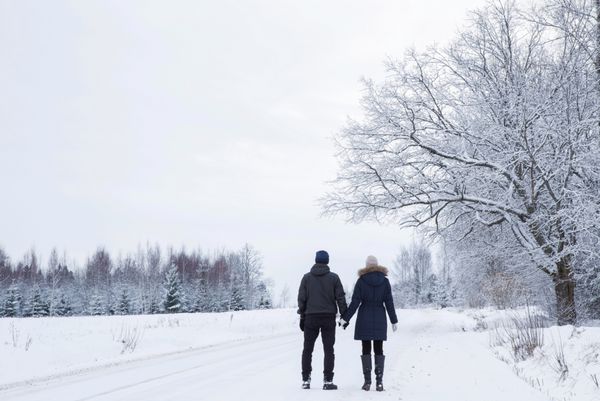 زن و شوهر در حال راه رفتن در جاده های برفی سفید شاخه های درخت و صنوبر پوشیده از برف هستند و بسیار زیبا به نظر می رسند روز زمستان