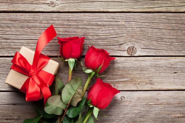 کارت تبریک روز گل رز قرمز و جعبه هدیه روی میز چوبی نمای بالا با sp برای تبریک شما