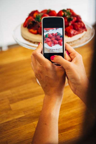 هنگام گرفتن کیک توت فرنگی روی پایه تلفن همراه را در دست گرفته اند