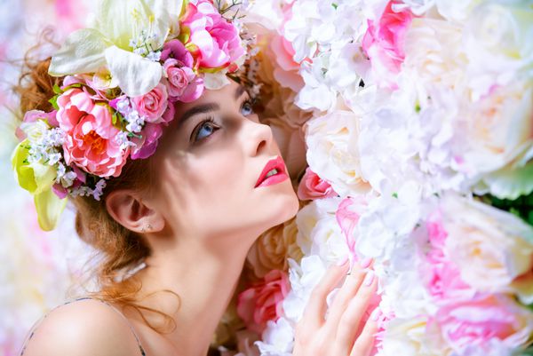 زن جوان عاشقانه زیبا در تاج گلی که روی پس زمینه گل رز ژست گرفته است الهام بخش بهار و تابستان مفهوم عطر لوازم آرایشی