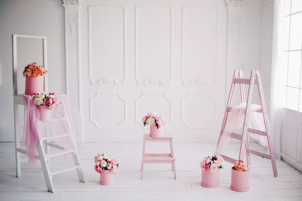 فضای داخلی سفید روشن با تعداد زیادی گل صورتی پودر صورتی دسته گل های صورتی ظریف در جعبه های گرد پله ها و صندلی روی کف چوبی سفید با تعداد زیادی دسته گل های صورتی