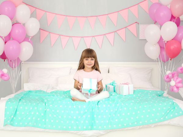 دختر تولد ناز با جعبه هدیه روی تخت نشسته است
