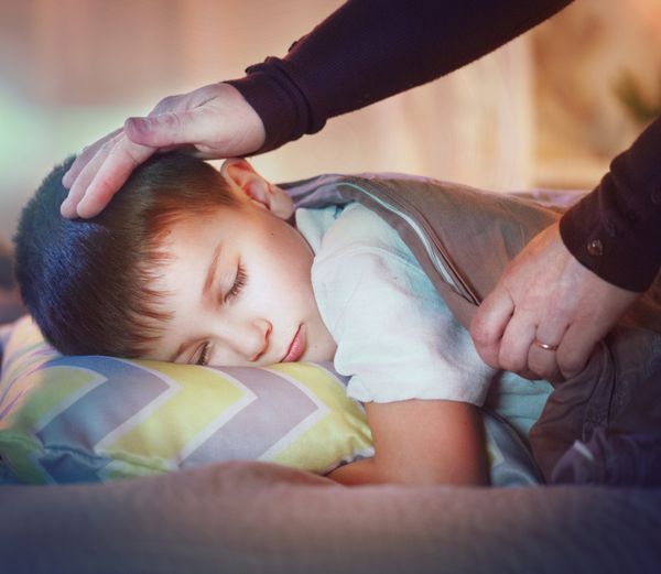 کودکی که در رختخوابش می خوابد و رویا می بیند مادر پسر کوچکش را با پتو می پوشاند دست زدن مادر روی سر کودک مفهوم کودکی و والدینی گرما و مراقبت های بهداشتی